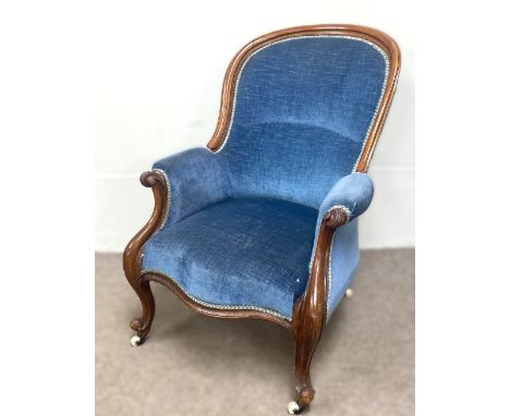 A Victorian spoon backed mahogany armchair, with padded back and seat, and cabriole front legs with castors, currently uphols