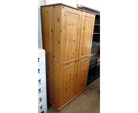 A 3' 1" modern waxed pine double wardrobe with shelf and hanging space enclosed by a pair of panelled doors, set on bun feet