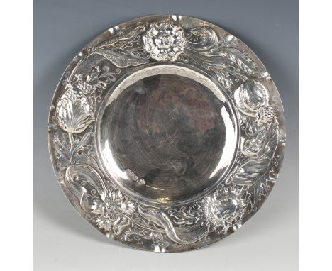 A late Victorian Arts and Crafts silver circular plate, the wide rim embossed with flowers, seed heads and leaves, London 189