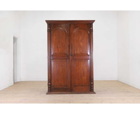 A teak or padouk wardrobe,mid-19th century, Anglo-Indian, the moulded frieze over twin arched panelled doors, flanked by ring