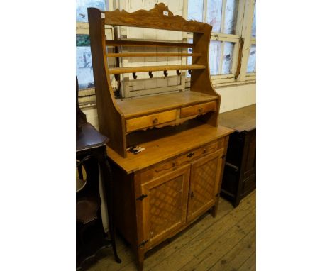 An early 20th century light oak folk art dresser with plate rack back, having four drawers and two panelled cupboard doors 