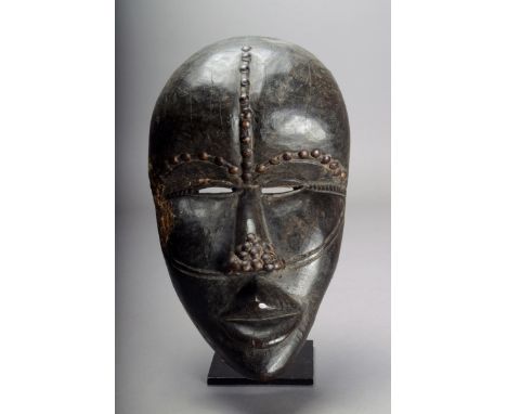 A Dan mask Ivory Coast wood with applied brass studs and with pierced eyes, 27.5cm high. Provenance Ian Auld, London.