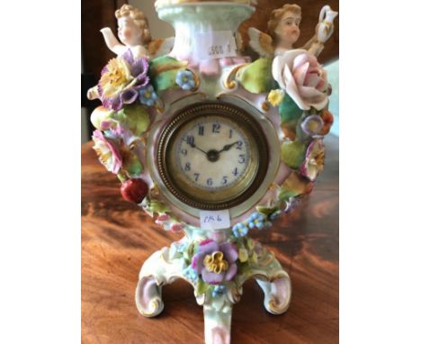 A DRESDEN PORCELAIN CLOCK CASE the central clock face surrounded by a floral encrusted case, two reclining cherubs to the sho