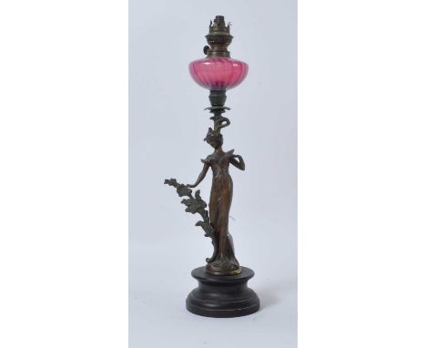 A late 19th century figural spelter oil lamp, having cranberry glass font and mounted upon an ebonised socle plinth, h.54cm