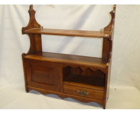 An Edwardian oak wall mounted open shelf with single drawer and cupboard enclosed by a small panelled door