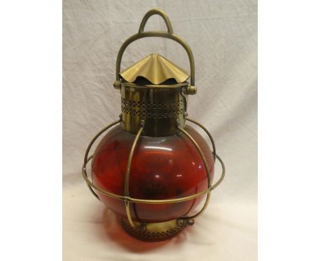 A brass ship's-style hanging light with spherical ruby-tinted glass lens, 18" high