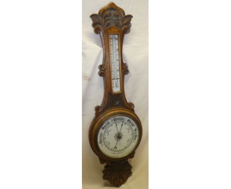 A good quality aneroid barometer with circular ceramic dial below thermometer in carved oak case