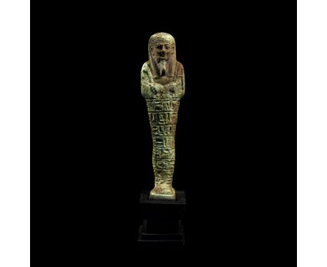 Late Period, 664-332 BC. A pale green composition shabti with tripartite wig and false beard, holding agricultural tools, a h