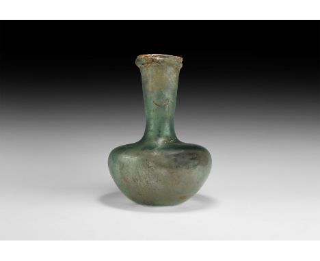 1st-2nd century AD. A green-aqua glass toilet bottle with dimple base, flared neck and carination below the mouth, rounded ri