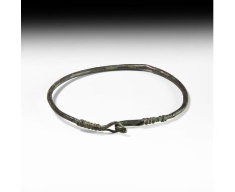 9th-12th century AD. A silver neck-ring formed as a round-section rod with ends coiled around the shank, hook-and-eye closure