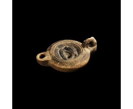 2nd century AD. A terracotta oil lamp with recessed discus decorated with a boar running left above a horizontal club, D-shap