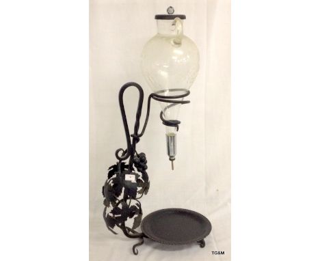 A vintage glass decanter with engraved decoration on a wrought iron stand
