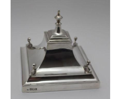 AN EDWARDIAN SILVER DESK INKWELL, hinged cover with urn finial, tapering to a square stepped base, pens holders in the round,