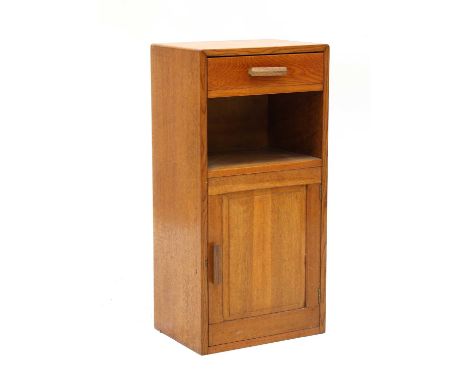 A Cotswold School oak bedside table, with a single drawer to the side, over a shelf, over a panelled cupboard door, opening o