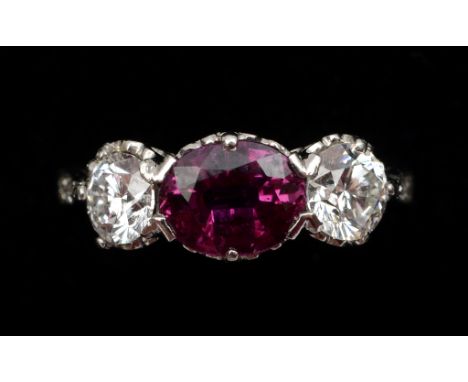 A ruby and diamond three stone ring, the central oval cut ruby flanked by brilliant cut stones, in a white coloured metal mou