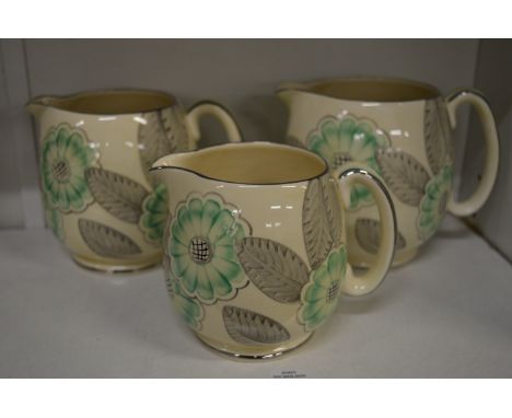 A graduated set of three Grays Pottery jugs decorated with flowers and leaves in green, grey and silver.