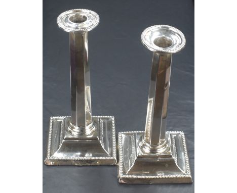A pair of Edwardian silver column candlesticks, with bead thread to the sconce rim and to the base, raised on a square step m
