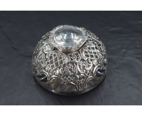 An Edwardian silver mounted glass inkwell, having a hinged cover over the pierced diaper and floral decorated silver mount, t