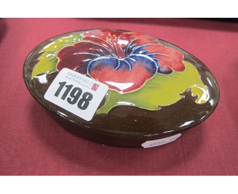 A Moorcroft Pottery Oval Trinket Jar with Lid, in the Hibiscus pattern on brown ground, 13cm wide.