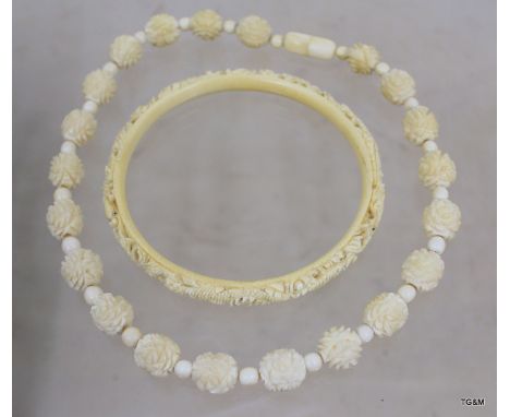 Large ivory bangle carved with dragons, 10cm in diameter, and an ivory necklace of carved floral beads 