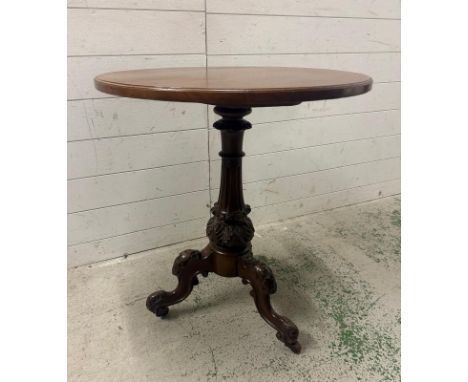 A circular mahogany pedestal table on heavily carved splayed tripod legs and ending on castors (H72cm Dia64cm)