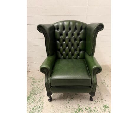 A green faux leather wingback chair with a button-tufted back, cabriole legs and brass stud detailing 