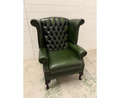 A green faux leather wingback chair with a button-tufted back, cabriole legs and brass stud detailing 