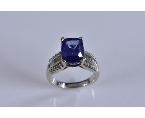 A tanzanite and diamond ring, oval cushion cut vibrant blue purple tanzanite approx 4.0ct, above baguette and round cut diamo