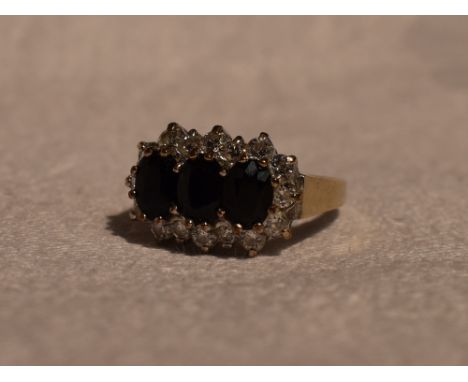 A lady's dress ring having a trio of sapphires within a cubic zirconia border in a stepped claw set mount on a 9ct gold loop,