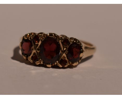 A lady's dress ring having a trio of garnets interspersed by garnet chips in a gallery mount on a 9ct gold loop, size R &amp;