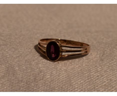 A lady's dress ring having an oval ruby style stone in a collared mount to open triple bar shoulders on a yellow metal loop s