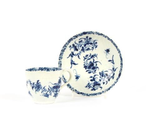 An 18th Century Worcester tea cup and saucer, with floral decoration and leaf moulded ground, under-glazed blue crescent mark