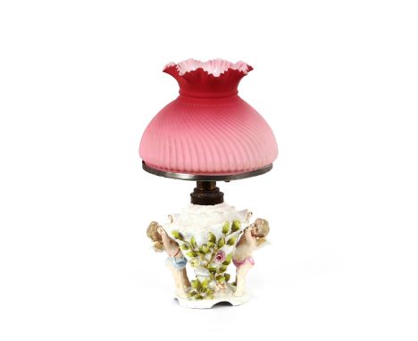 A 19th Century continental porcelain table lamp,&nbsp;decorated cherubs and flowers, with pink fluted and crimped satin glass