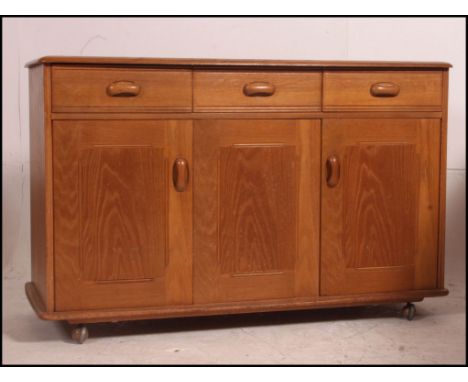 A 1970's retro Ercol style sideboard raised on ball castors with thin plinth having metamorphic cupboards under short drawers