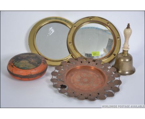 A brass framed convex mirror together with another brass porthole mirror, a brass school bell with ceramic handle, papier mac