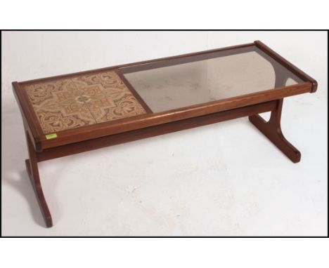 A G plan teak coffee table of rectangular form, the top inset by floral tiles and inset smoke glass panel raised on shaped su