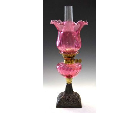 Cranberry oil lamp raised on a square cast metal base, 54cm high