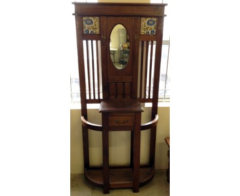 An Art Nouveau/Art Deco style hall stand with 2 nouveau tiles inset, a central oval mirror, brass swan neck coat/hat hooks an