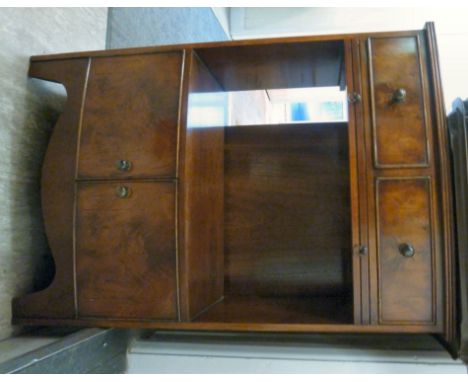 A mid 20thC yew wood finished bow front cabinet, having two in-line drawers, over a slide, on open compartment and a pair of 