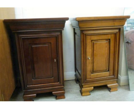 A pair of modern mahogany finished bedside cupboards of panelled design, each having a concealed frieze drawer, over a lockab