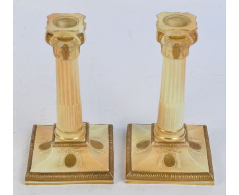 A pair of Royal Worcester blush ivory candlesticks modelled as Corinthian columns on spreading square bases, with gilt height