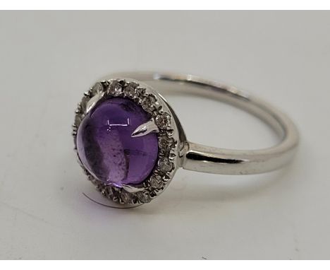 A 9ct. white gold, amethyst cabochon and diamond halo ring, set round cabochon amethyst to centre bordered by ring of numerou