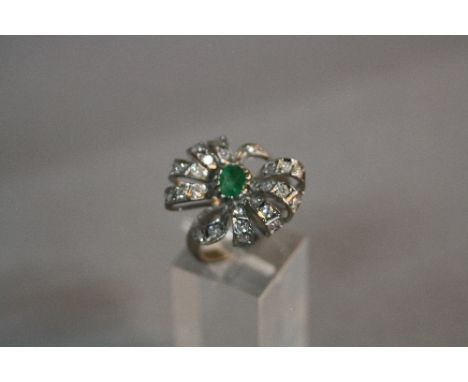 A MODERN EMERALD AND DIAMOND FANCY BOW DESIGN RING, one oval mixed cut emerald measuring approximately 6 x 4mm, estimated wei