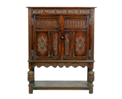 A 20th Century oak reproduction livery cupboard in the Jacobean style, with rosette carved frieze over double doors and carve