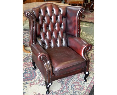 An ox blood leather wing back armchair, button upholstered back, scrolling arms, cabriole legs, club feet.