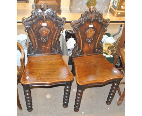 A pair of Victorian carved oak hall chairs, decorated with foliate scroll motifs to the back, on bobbin turned front legs.