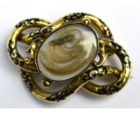 A large Victorian gold plated mourning brooch centred with an oval hair locket within black enamel decorated looping frame, w