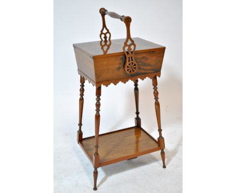 A circa 1900 walnut sewing box of rectangular tapering form with twin hinged top and swing handle on four ring turned support