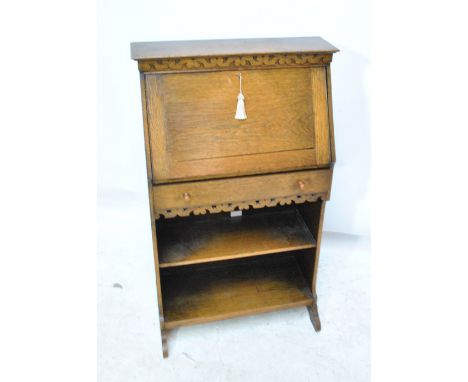 An early 20th century oak students bureau with fretwork carved frieze, sectioned interior, single drawer, shelf and outswept 