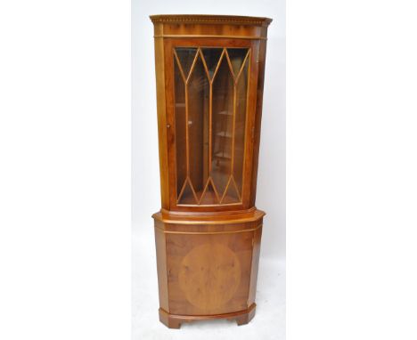 A reproduction yew wood freestanding corner cupboard with astragal glazed upper section above cupboard base to bracket feet, 